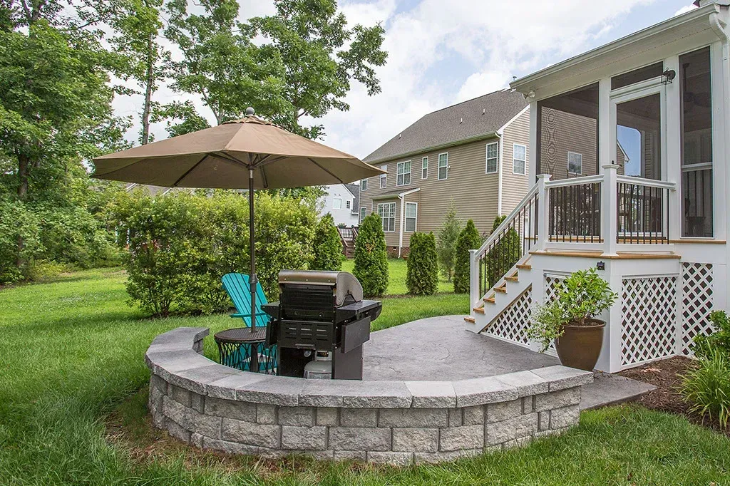 Backyard patio with grill, umbrella, and seating next to a screened porch.