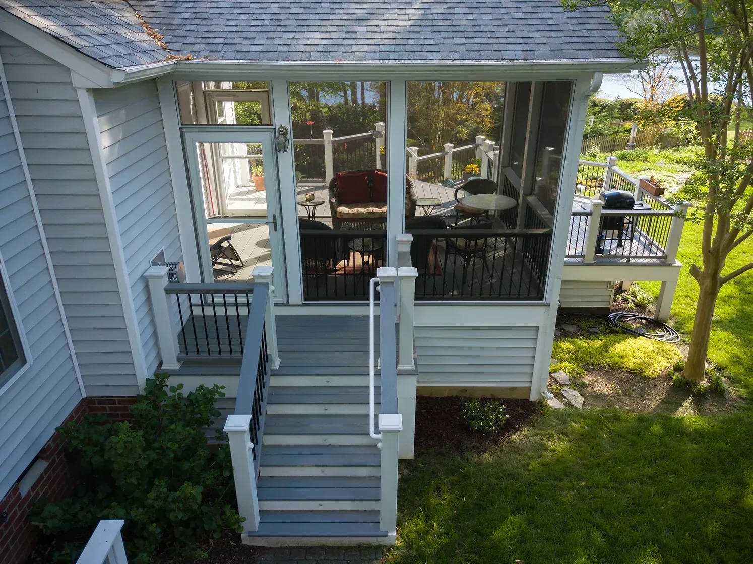 Light blue house with screened porch and stairs leading to it, green lawn.
