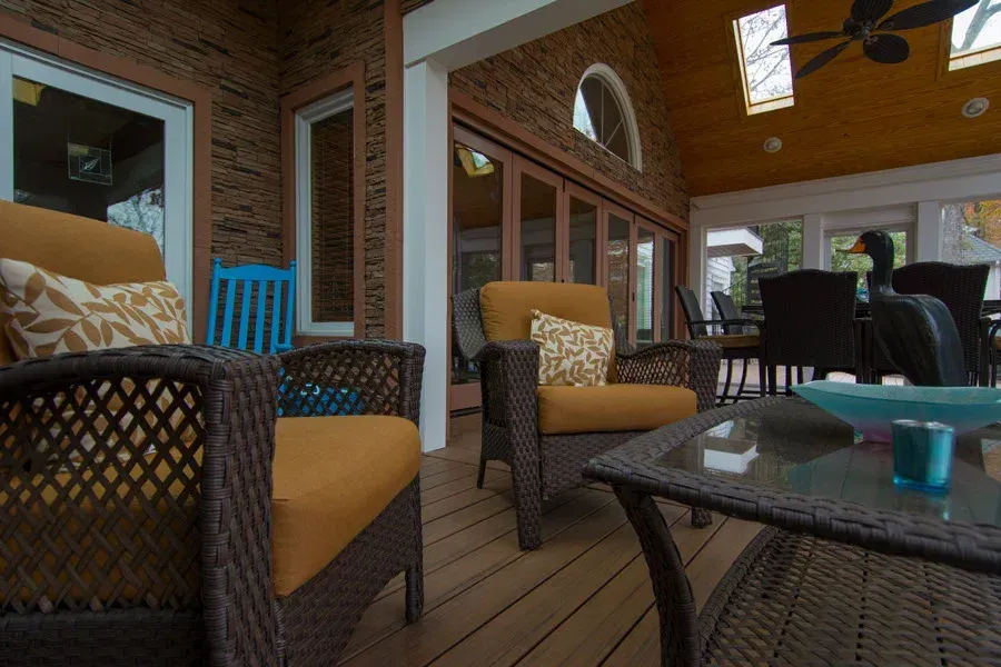 Outdoor seating area with wicker furniture and yellow cushions. Brick wall and wooden deck.