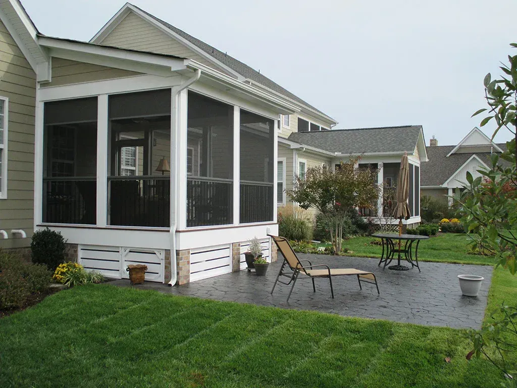 Screened-in porch on a house with patio, green grass, and lawn chair outside.