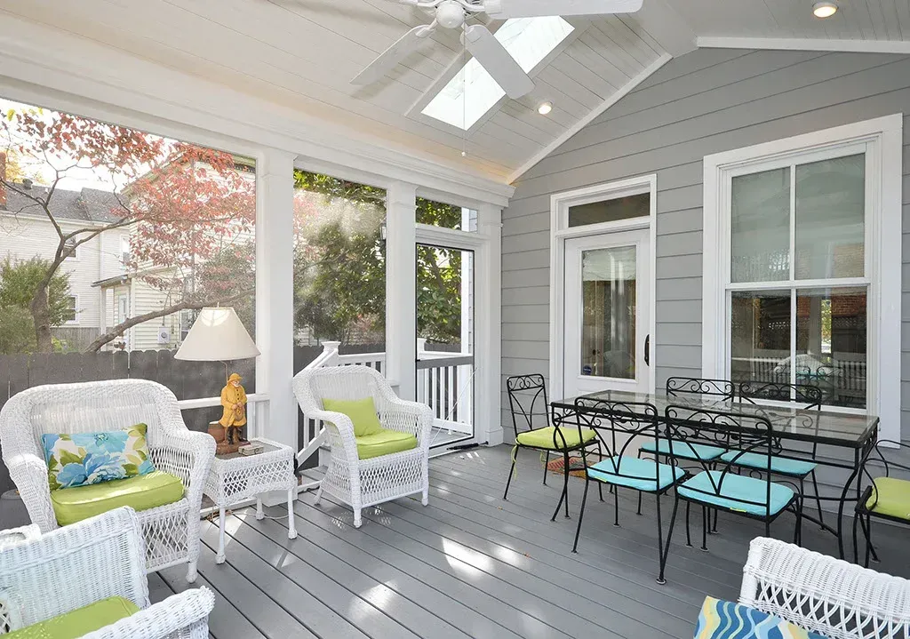 Screened porch with white wicker furniture, dining table, and gray walls.