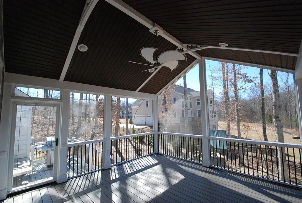 Sunlit screened-in porch with dark ceiling, white trim, and a view of trees and houses.