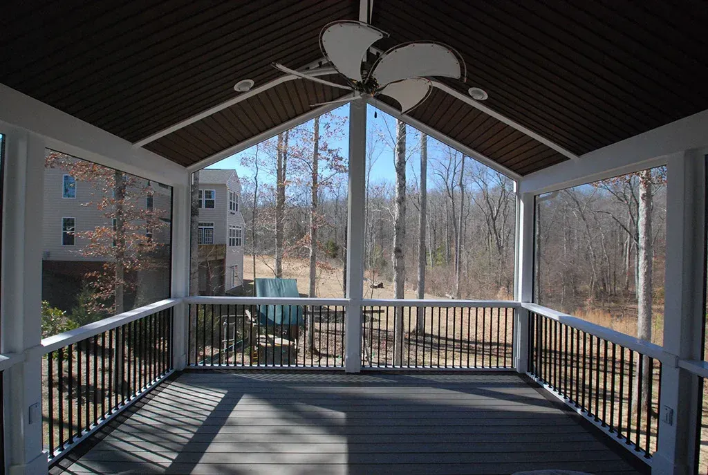 Screened-in porch with dark railing and ceiling. Views of trees and distant building through the screened walls.