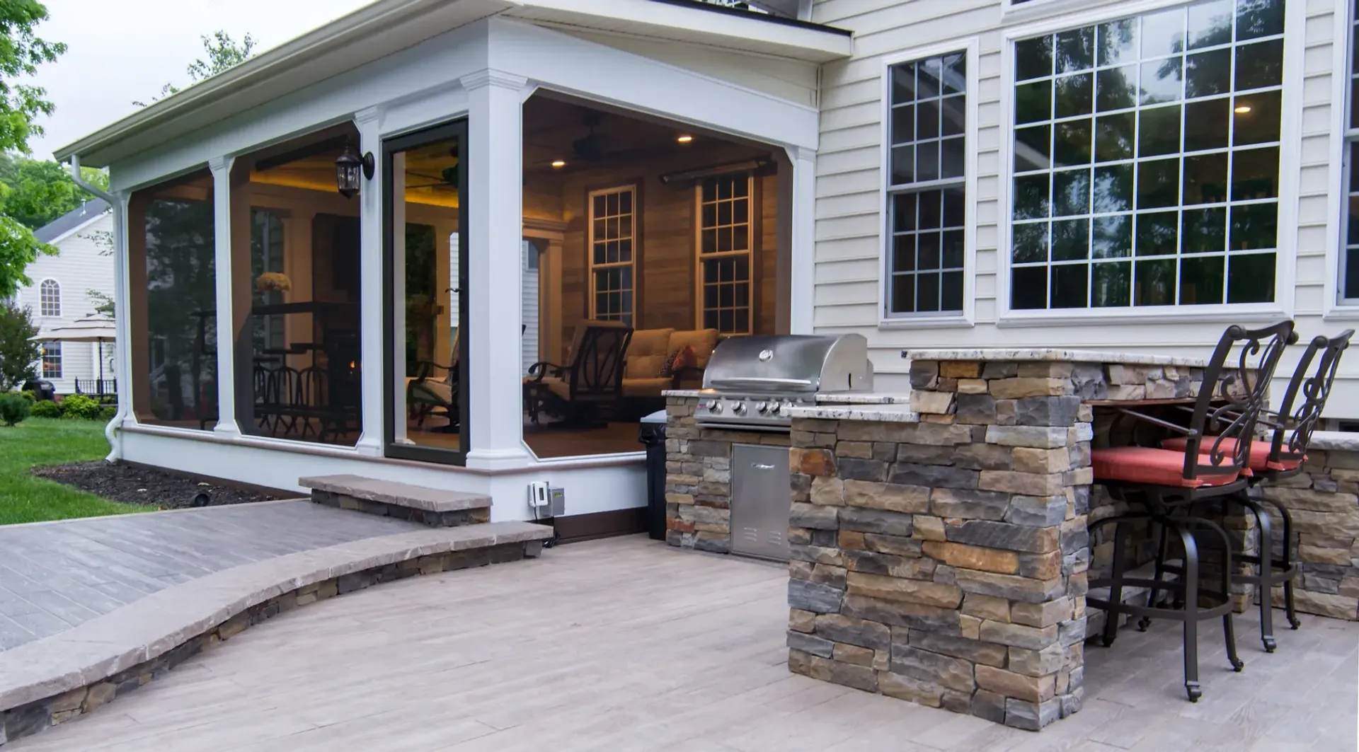 Outdoor patio with stone grill island, screened porch, and brick walkway.