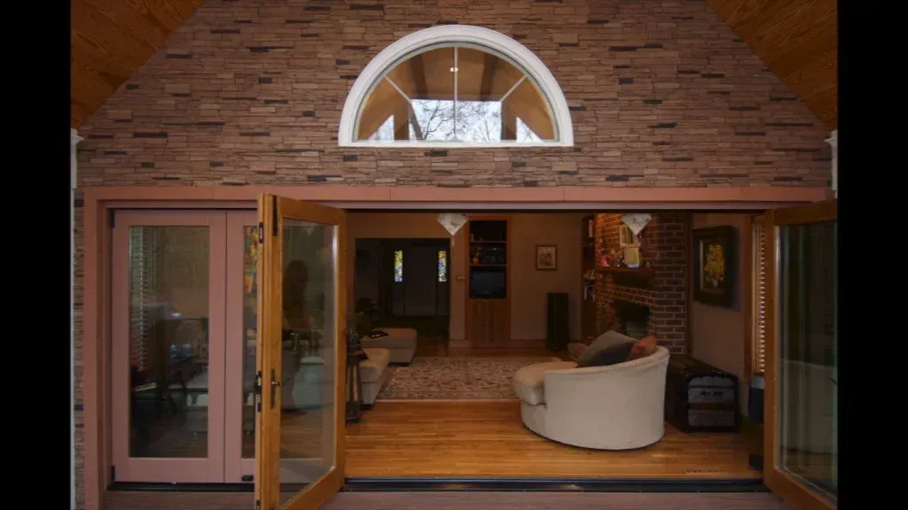 Open doors reveal a living room. Exterior has stone wall, arched window.