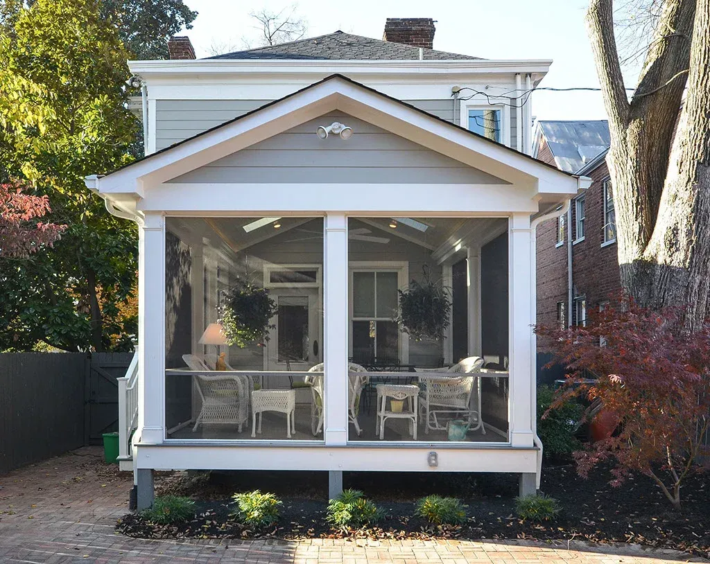 Gray and white screened porch with white furniture. Brick walkway and landscaping in front.