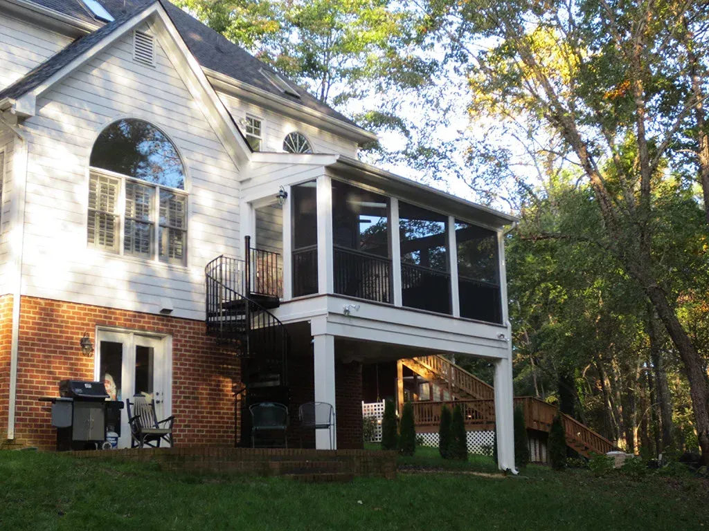 A two-story house with a screened porch and spiral staircase. Overcast, exterior shot.