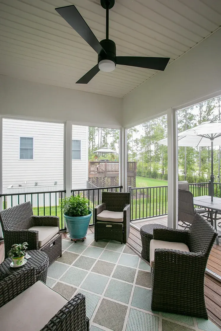 Screened-in porch with wicker furniture, a ceiling fan, and a colorful patterned rug.