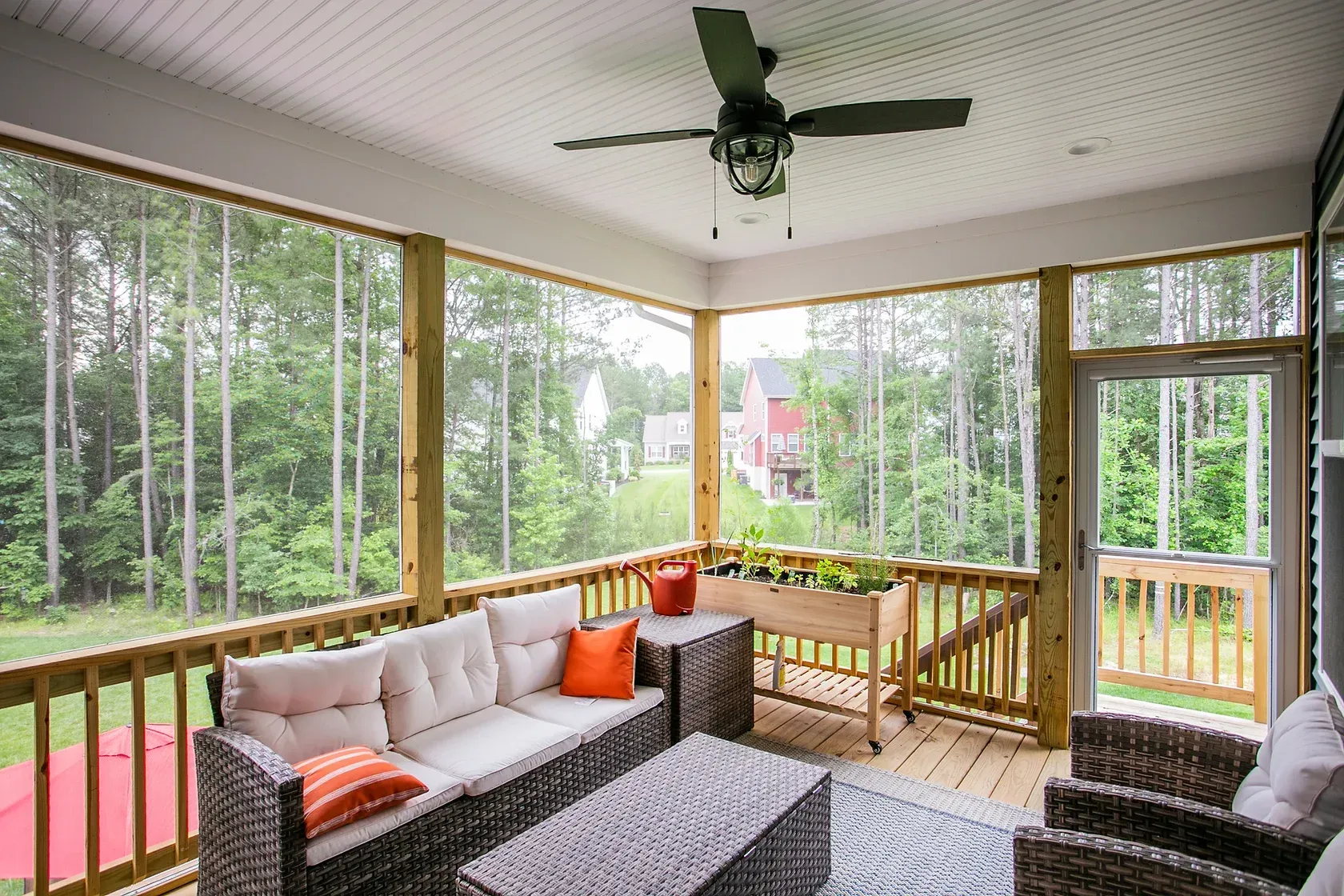 Screened-in porch with outdoor furniture, ceiling fan, and garden box, overlooking a backyard with trees.