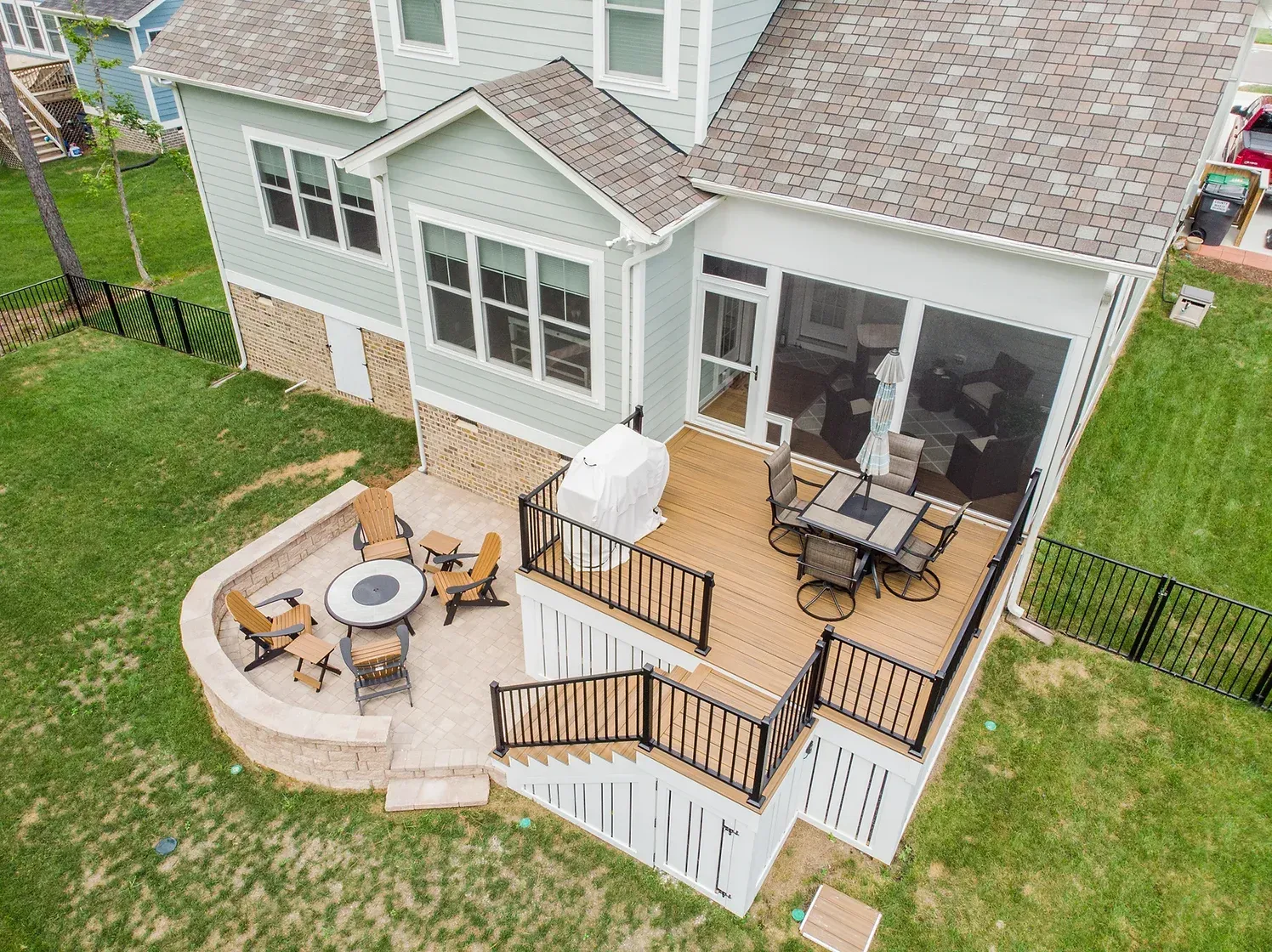 Backyard deck with fire pit and dining area, attached to a light blue house.
