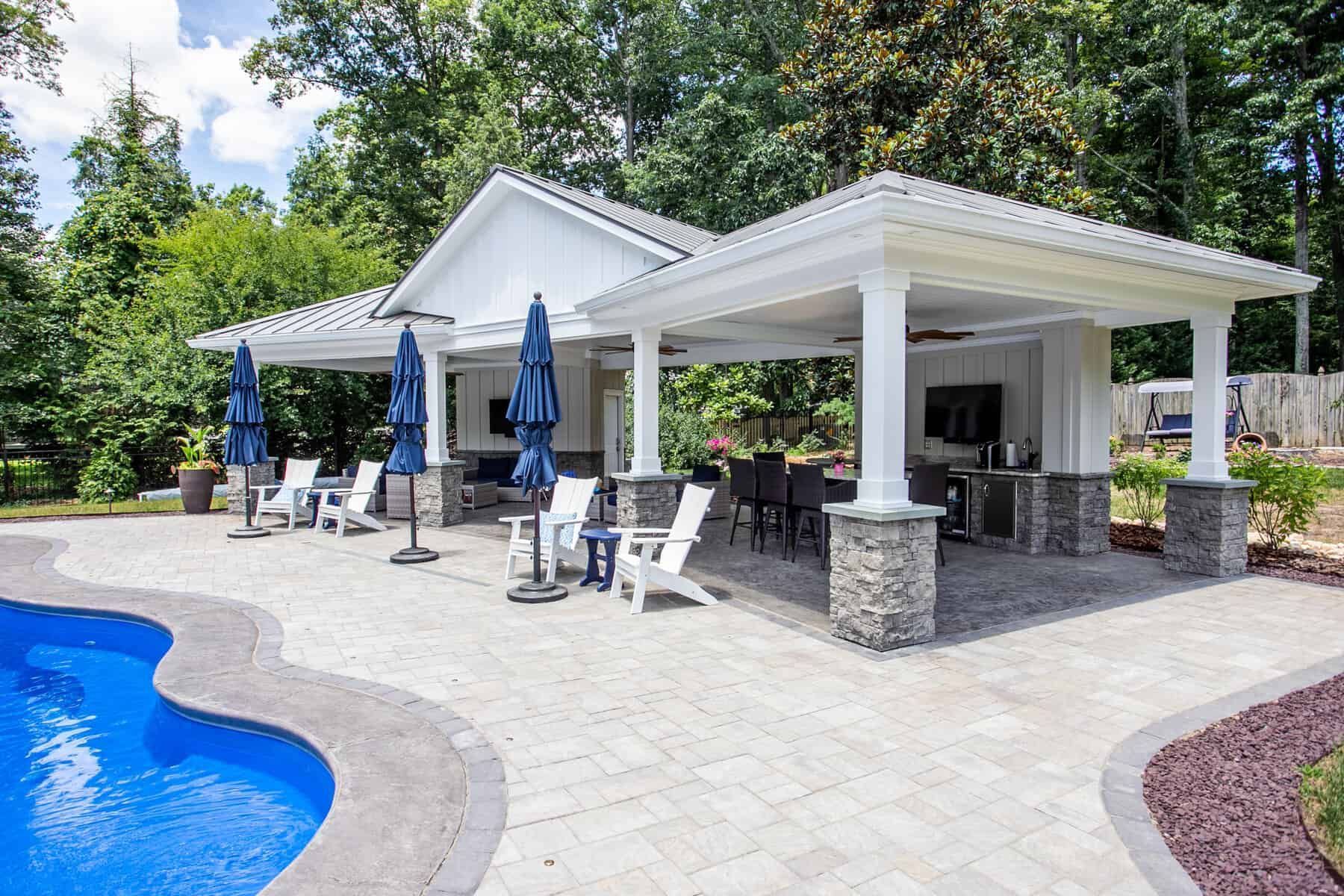 Poolside pavilion with blue umbrellas, lounge chairs, and outdoor kitchen.