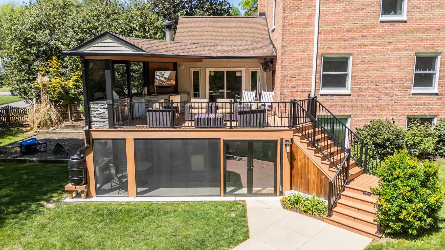 Backyard deck with screened-in porch, seating, and stairs leading to a brick building.