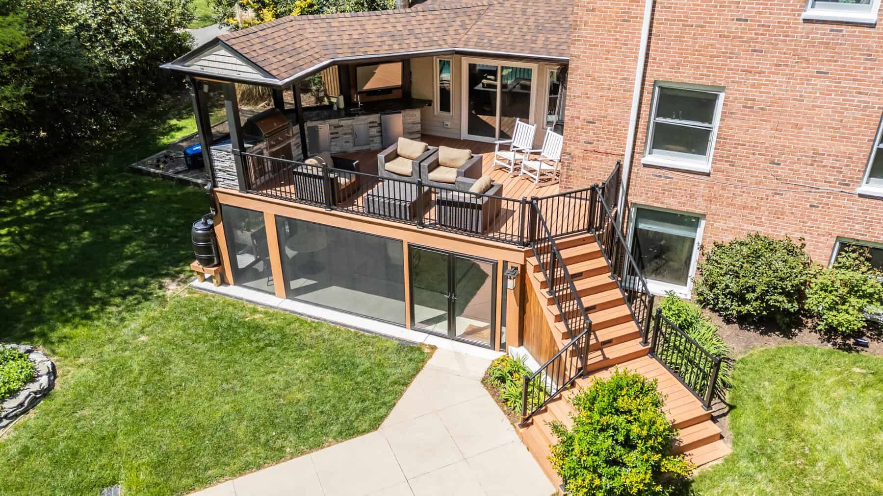 Aerial view of a multi-level wooden deck with a screened-in section, stairs, and outdoor seating next to a brick house.