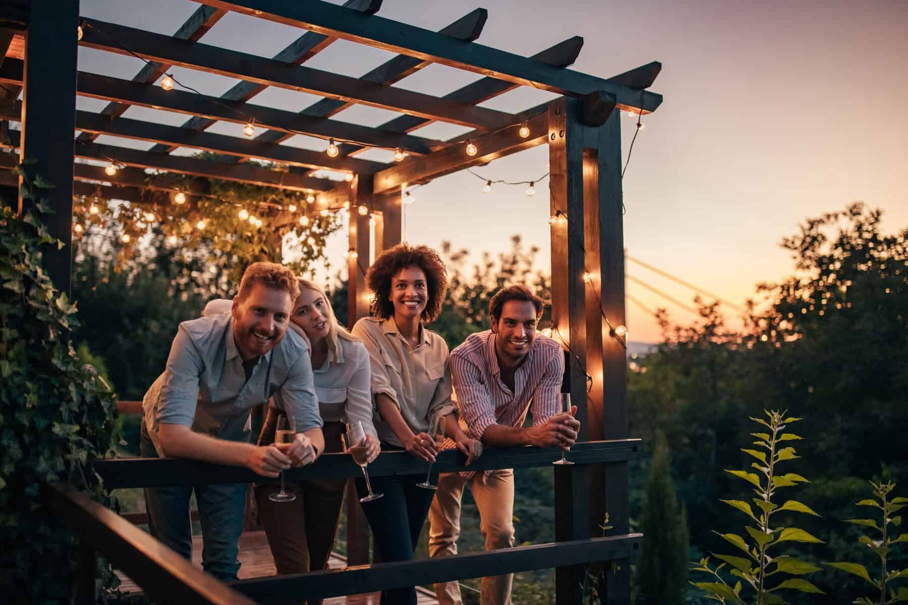 Friends gathered under a pergola with string lights, smiling at sunset.