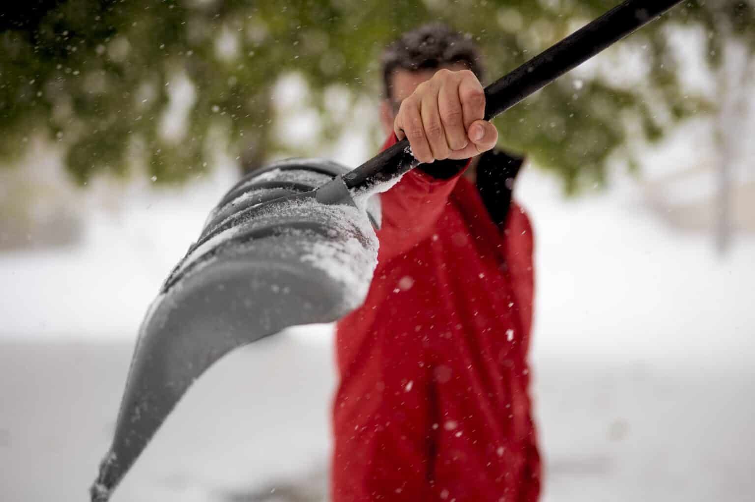 Person in red coat shovels snow, blurred background.