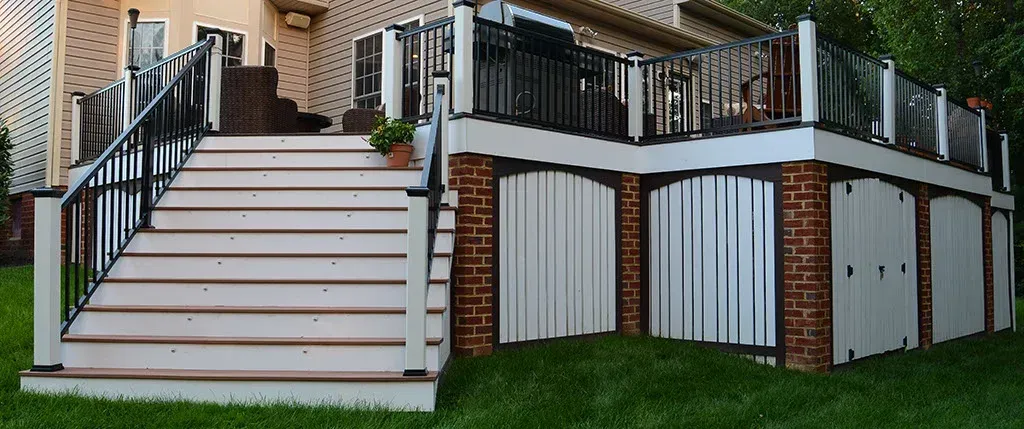 Deck with stairs, white siding, black railing, and brick accents against green grass.