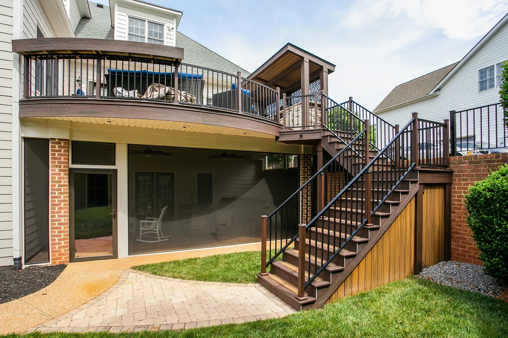 Backyard deck with stairs to a screened porch below. Brown wood and black railing. Sunny day.