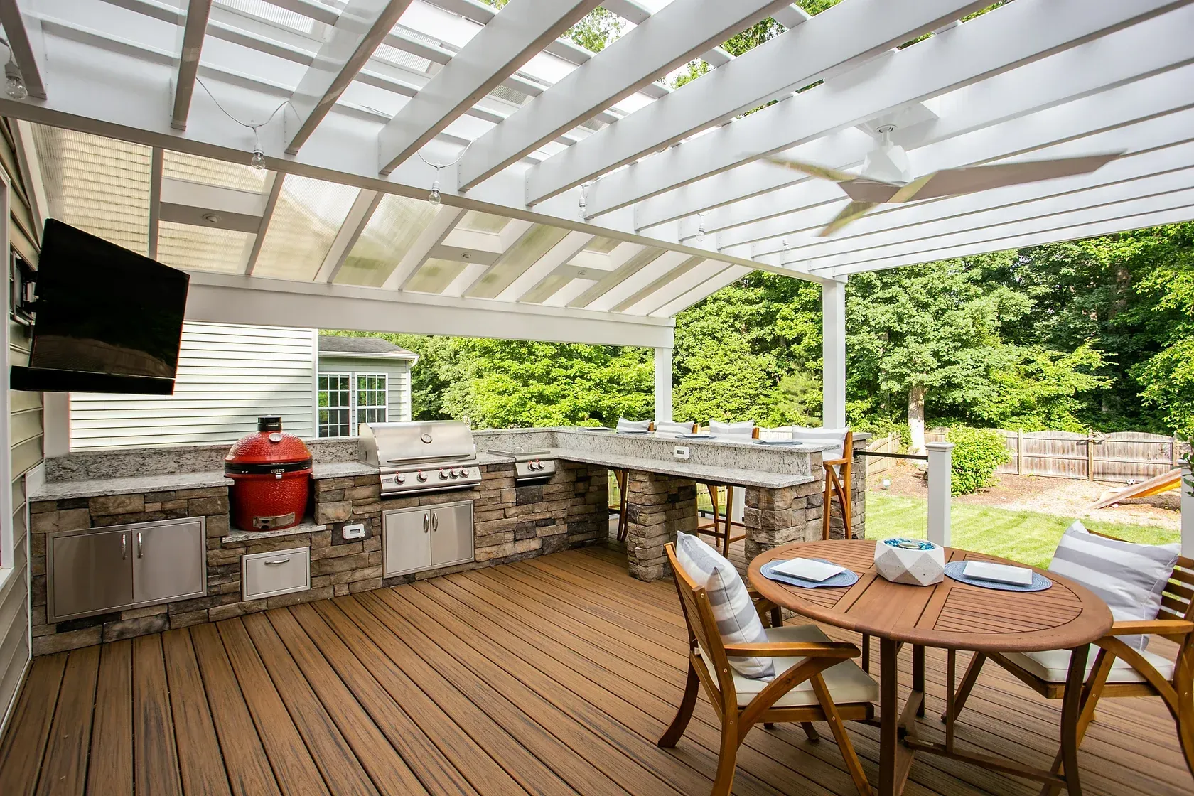 Outdoor kitchen with grill, countertop, table, and seating under a pergola.