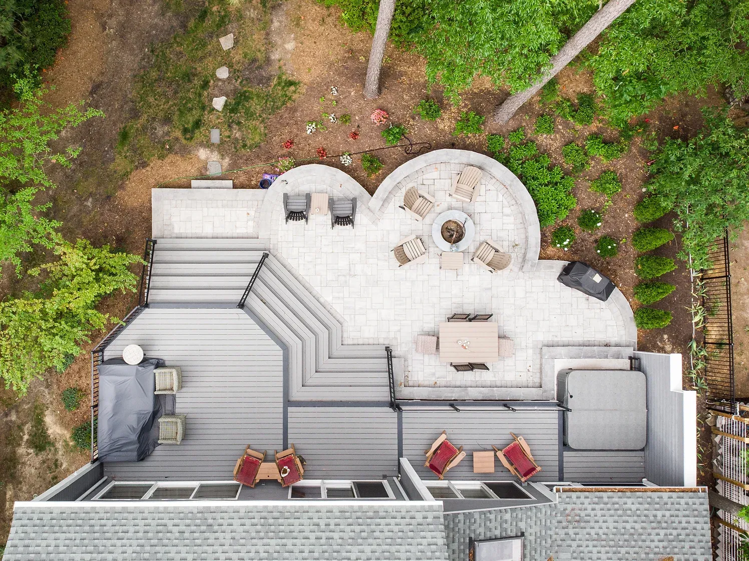 Overhead view of a multi-level outdoor patio with seating, fire pit, hot tub, and deck, surrounded by trees.