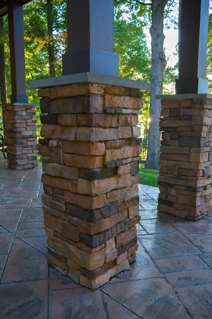 Stone-covered support columns on a patio, with trees in the background.