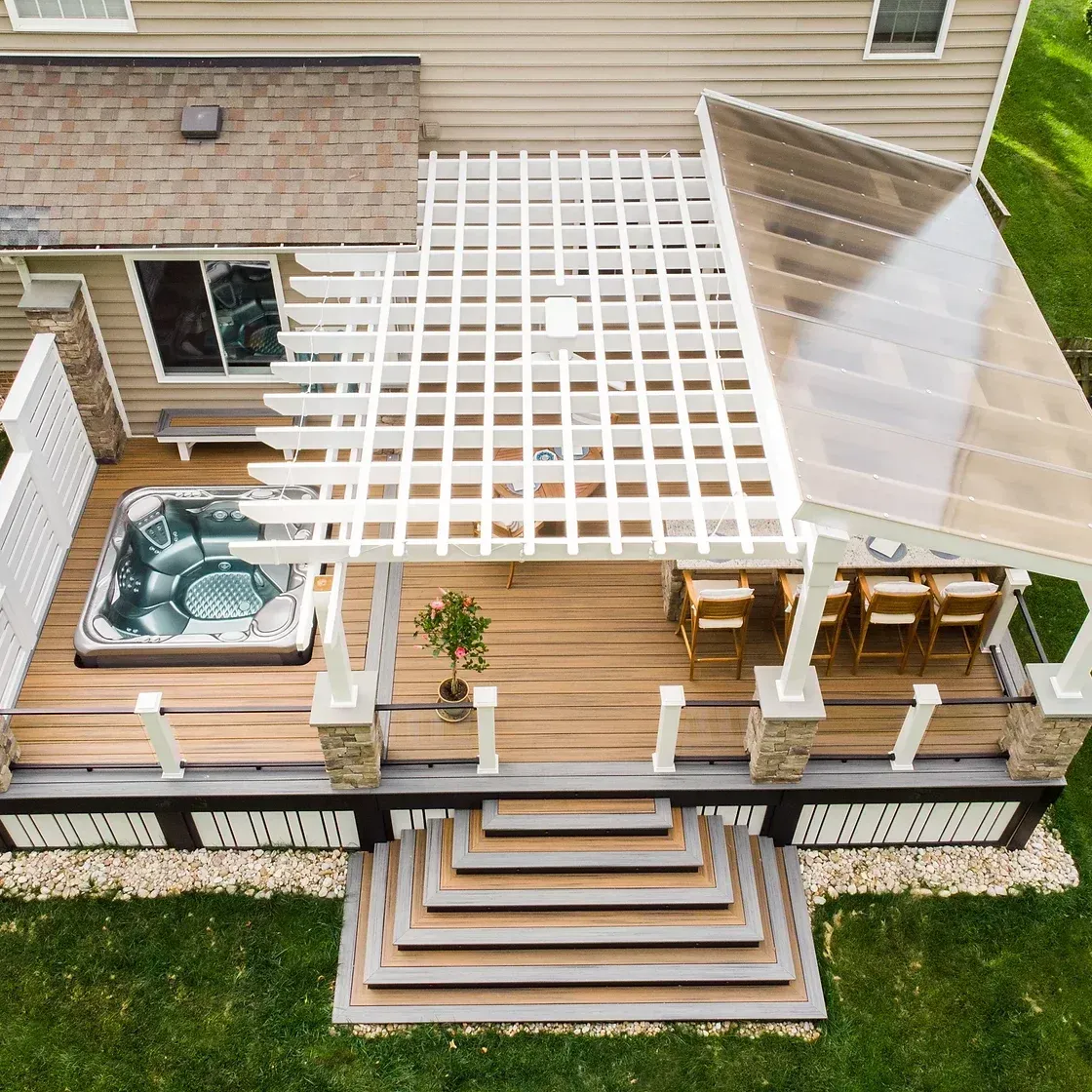 Overhead view of a deck with a hot tub, seating, pergola, and steps. Tan and white tones, with green grass.