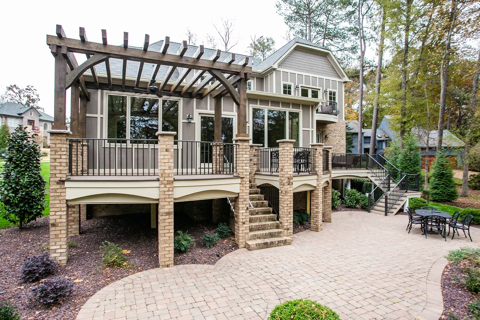 Exterior view of a house with a raised deck, pergola, and brick patio.