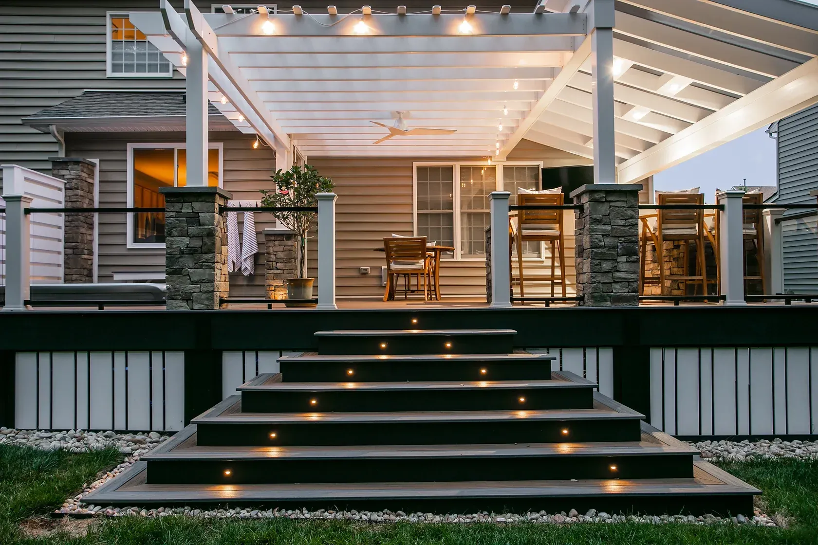 Wooden deck with steps lit by small lights, leading up to a covered patio with seating.