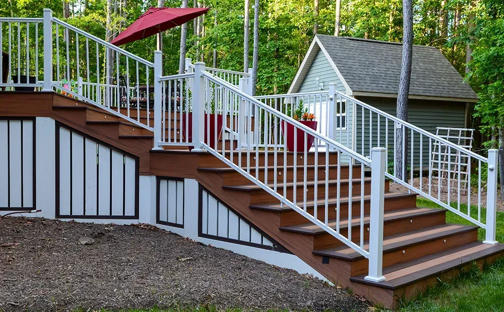 Outdoor staircase with white railing and brown steps leading to a deck with a red umbrella.