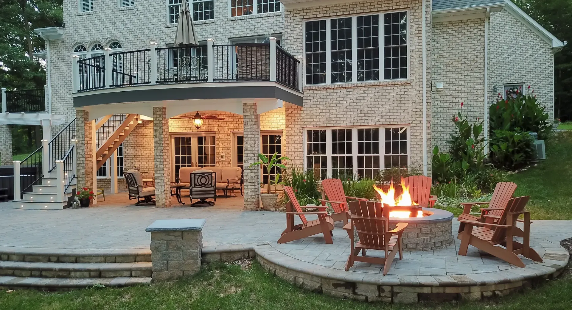 Backyard patio with fire pit, seating, and multi-level house with stone facade.