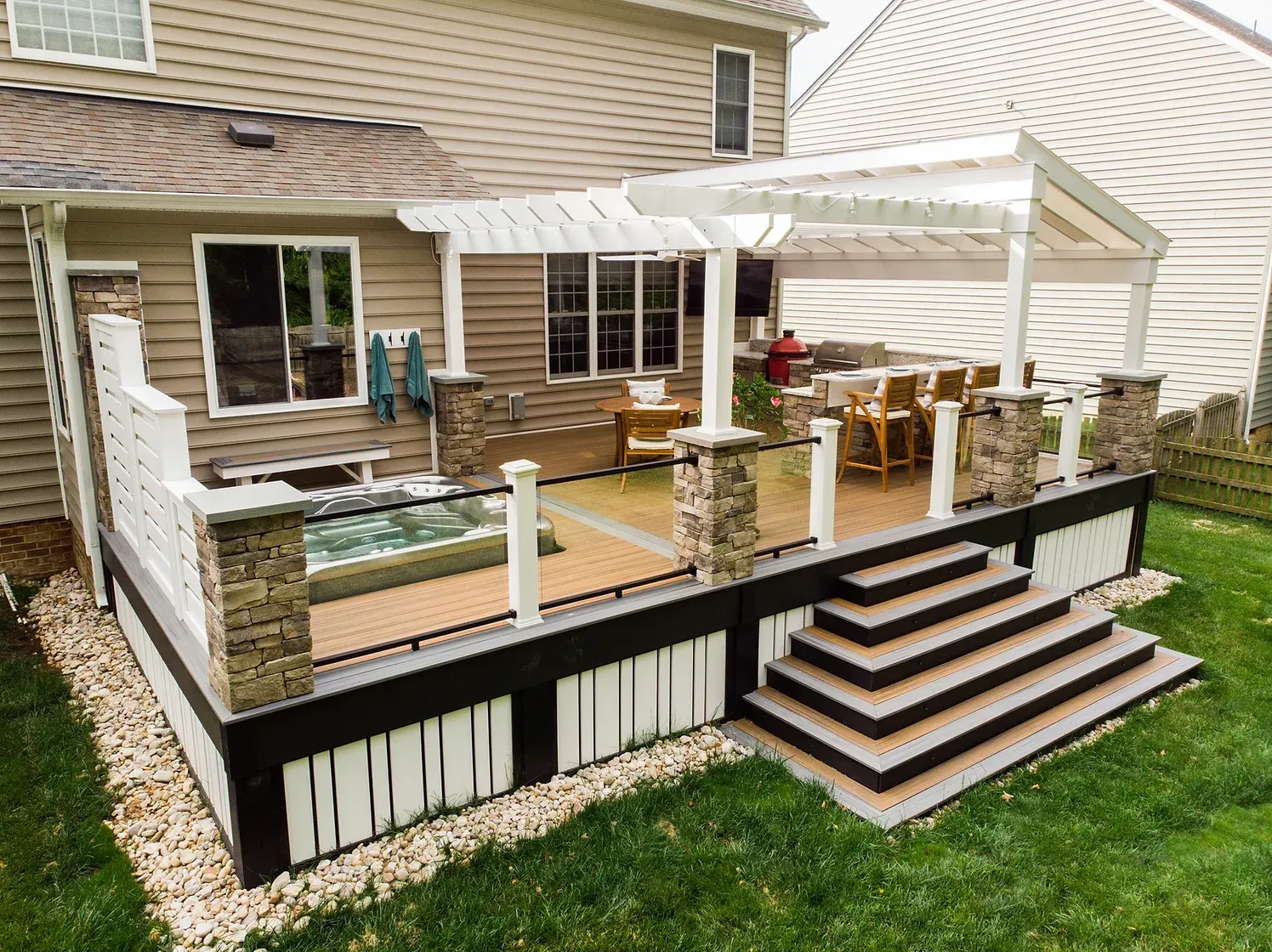 A multi-level outdoor deck with a pergola, hot tub, and steps surrounded by a lawn.