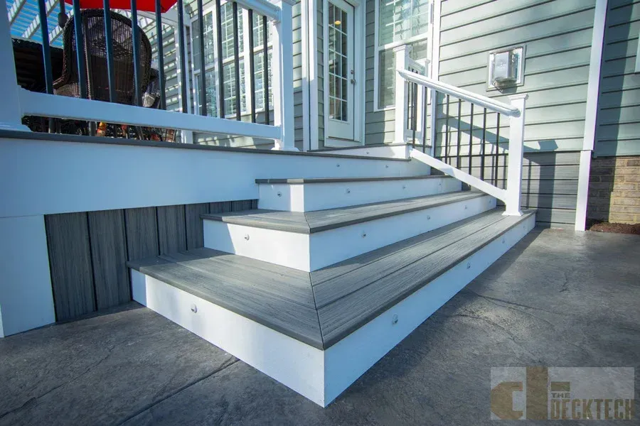 Outdoor steps with composite decking and white risers, leading up to a porch with railings.