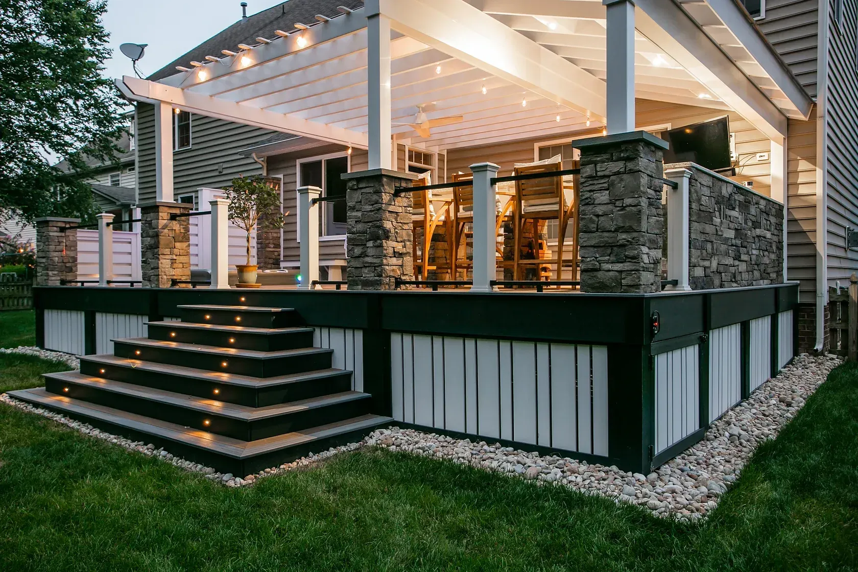 Outdoor deck with stone accents, pergola roof, steps with lighting, and glass railings.