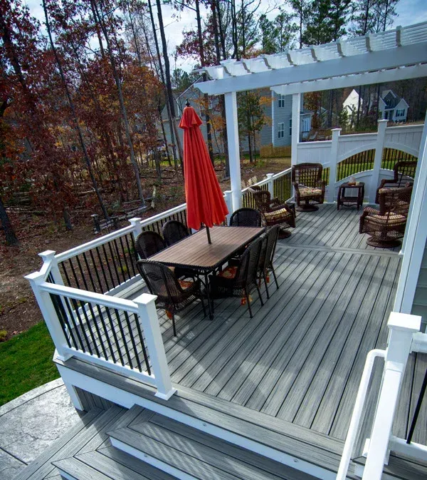 A wooden deck with patio furniture, including a table with a red umbrella, overlooking a wooded area.