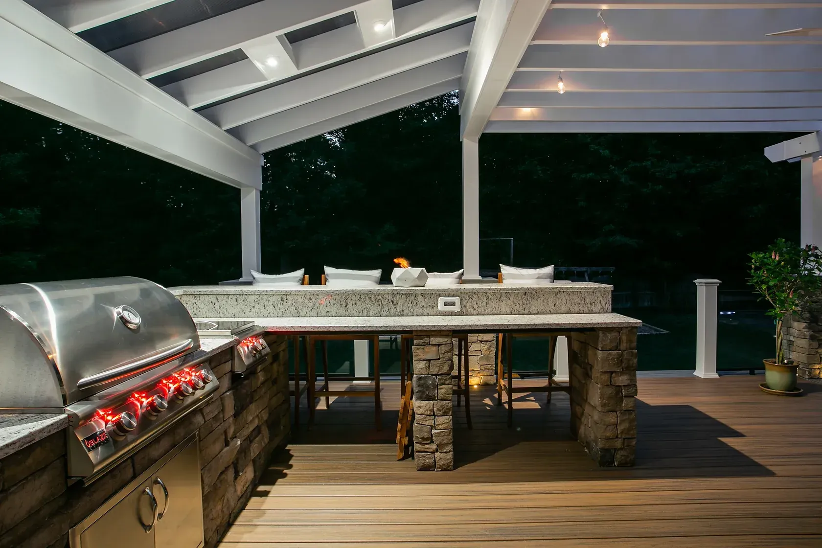 Outdoor kitchen with stainless steel grill, stone counter, and wooden deck.