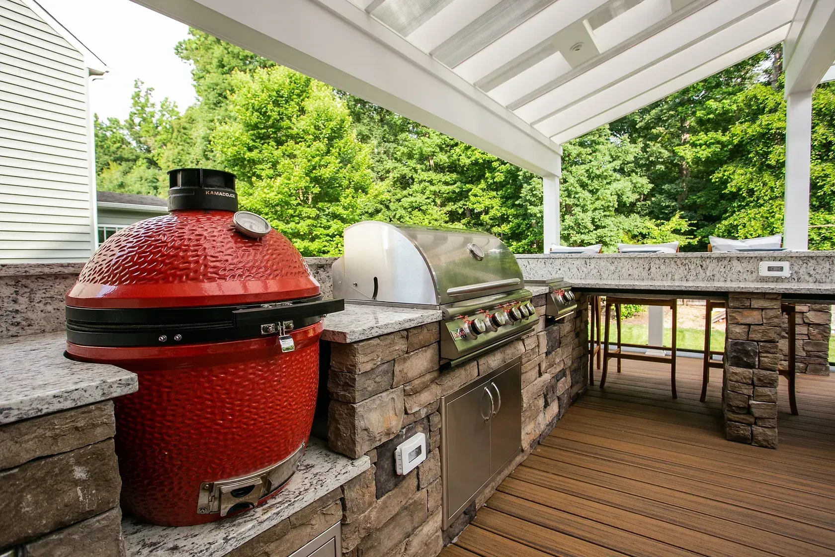 Outdoor kitchen with red ceramic grill, stainless steel grill, and granite countertops.