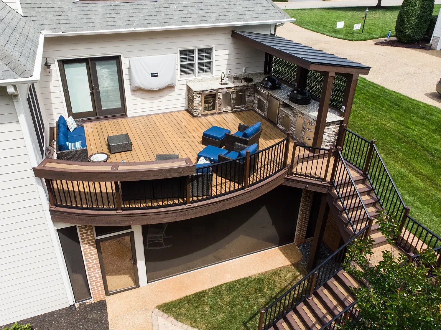 A multi-level outdoor deck with a kitchen, seating, and stairs, surrounded by green grass.