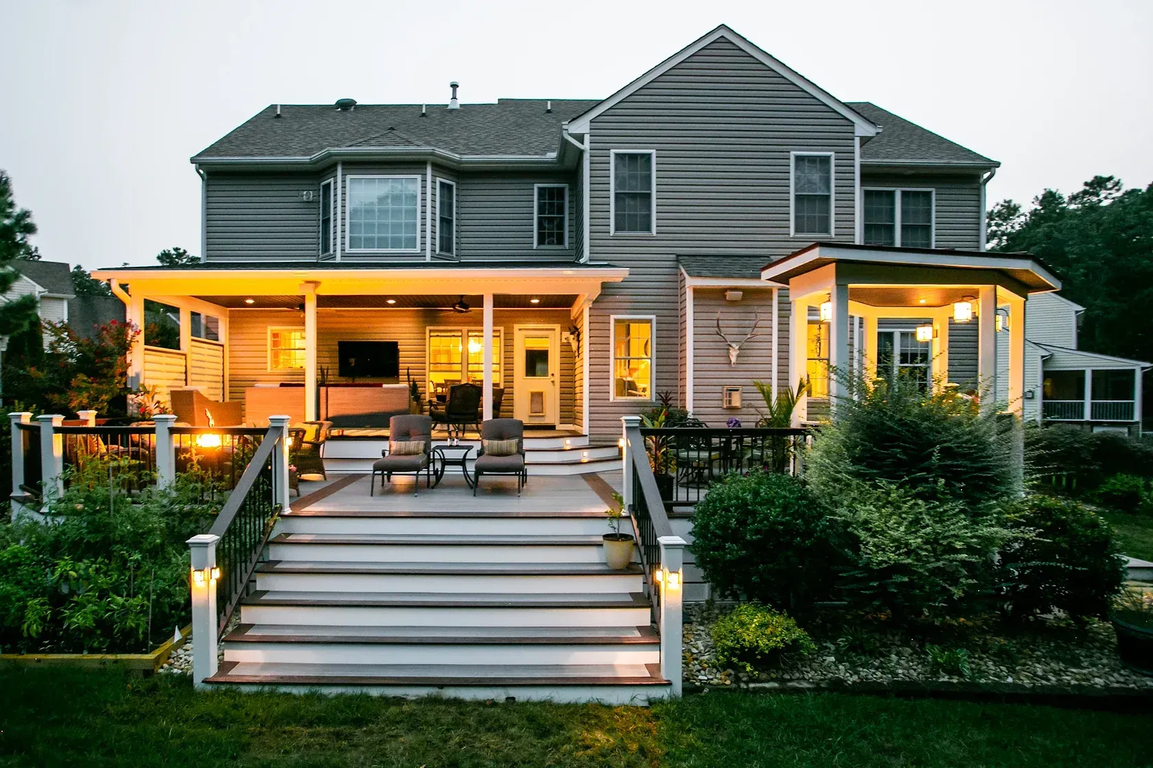 Backyard of a house with a deck and steps, lit up at dusk.