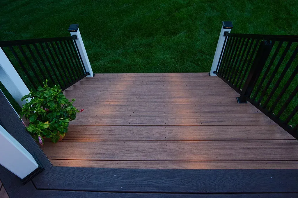 Wooden deck with black railing and potted plant, overlooking a green lawn.