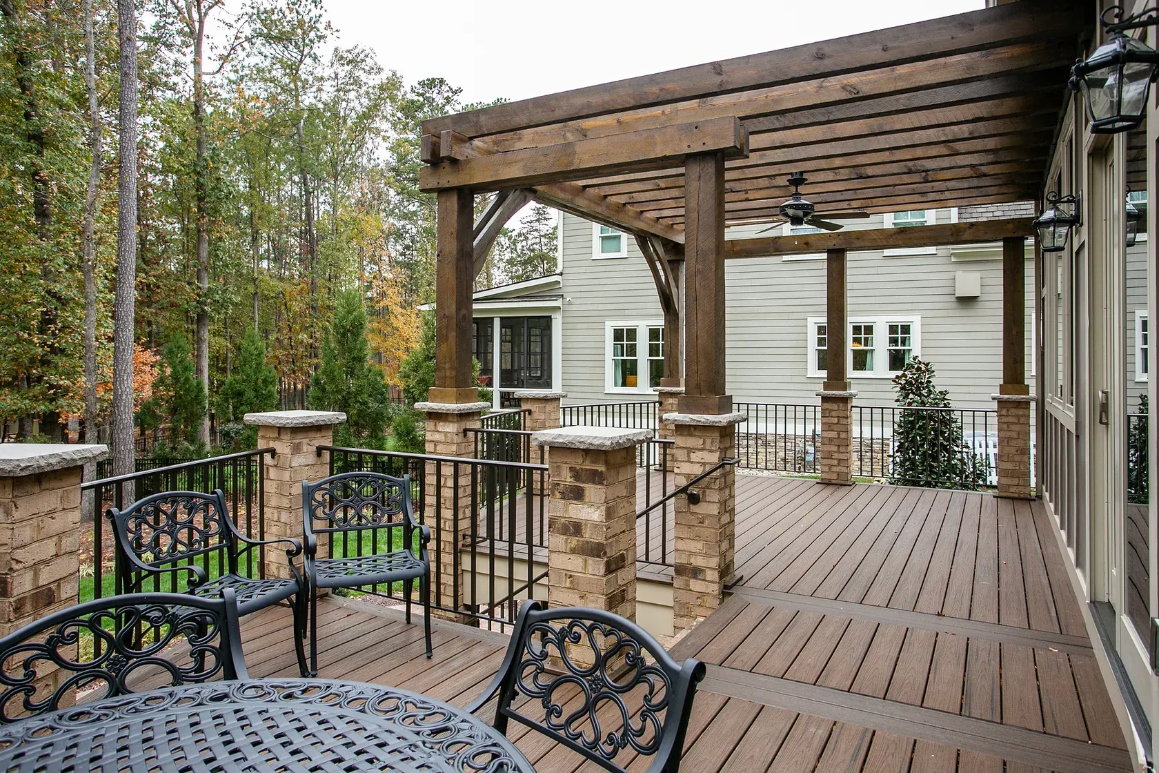 Outdoor deck with pergola, brick columns, metal chairs, and composite decking.