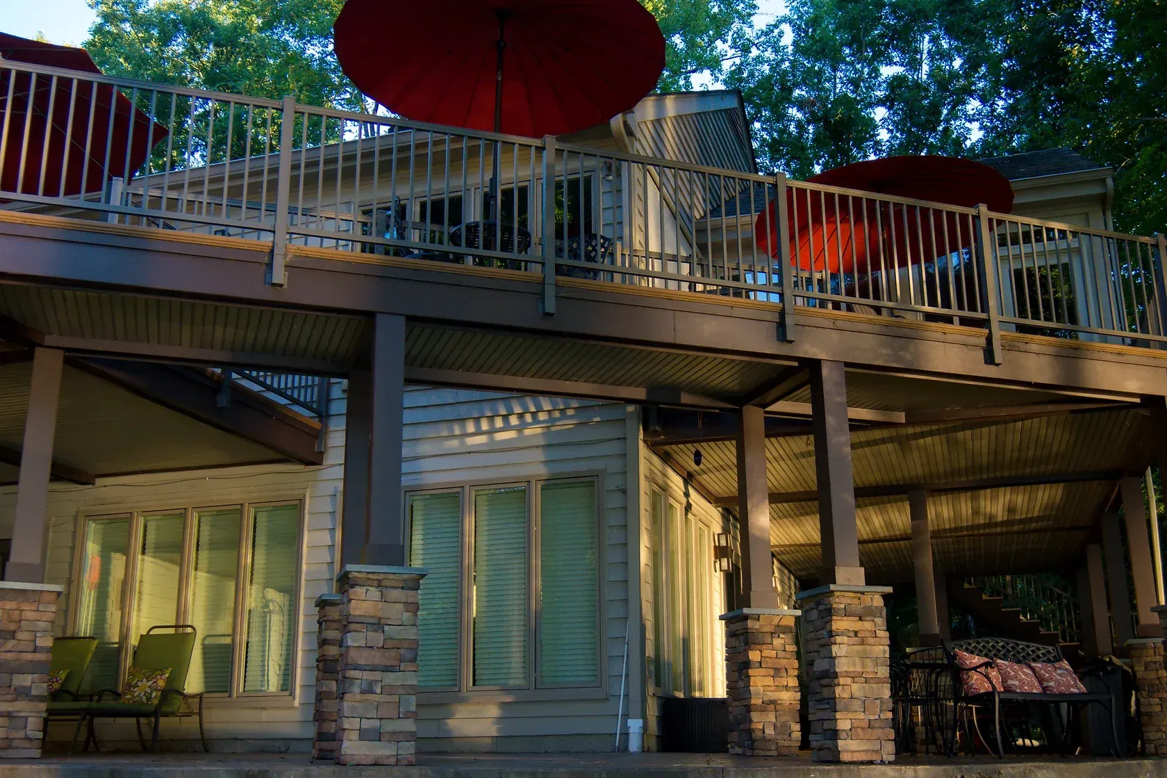 Lakeside house with a deck, red umbrellas, and chairs. Evening light bathes the building in warm tones.