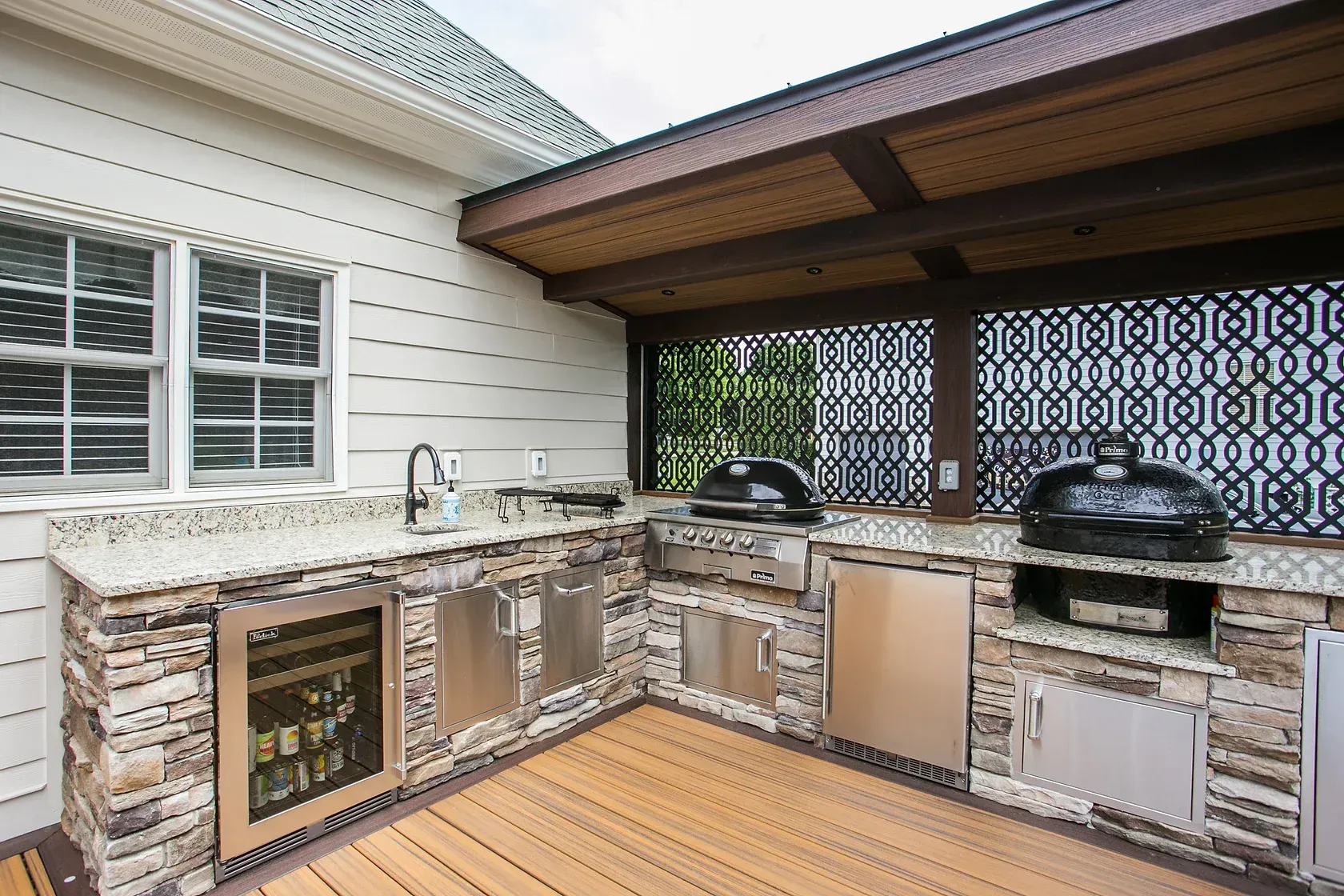 Outdoor kitchen with stone counters, stainless steel appliances, and built-in grill under a pergola.