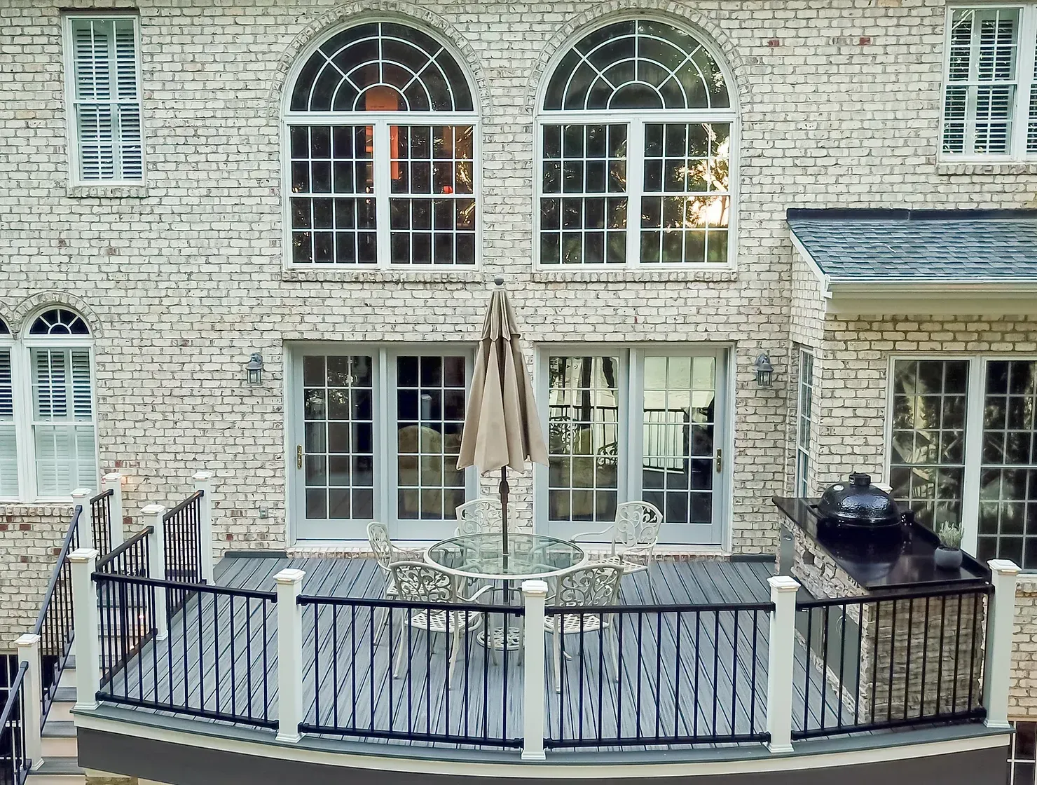 Backyard deck with furniture and umbrella, against a brick building with large arched windows.