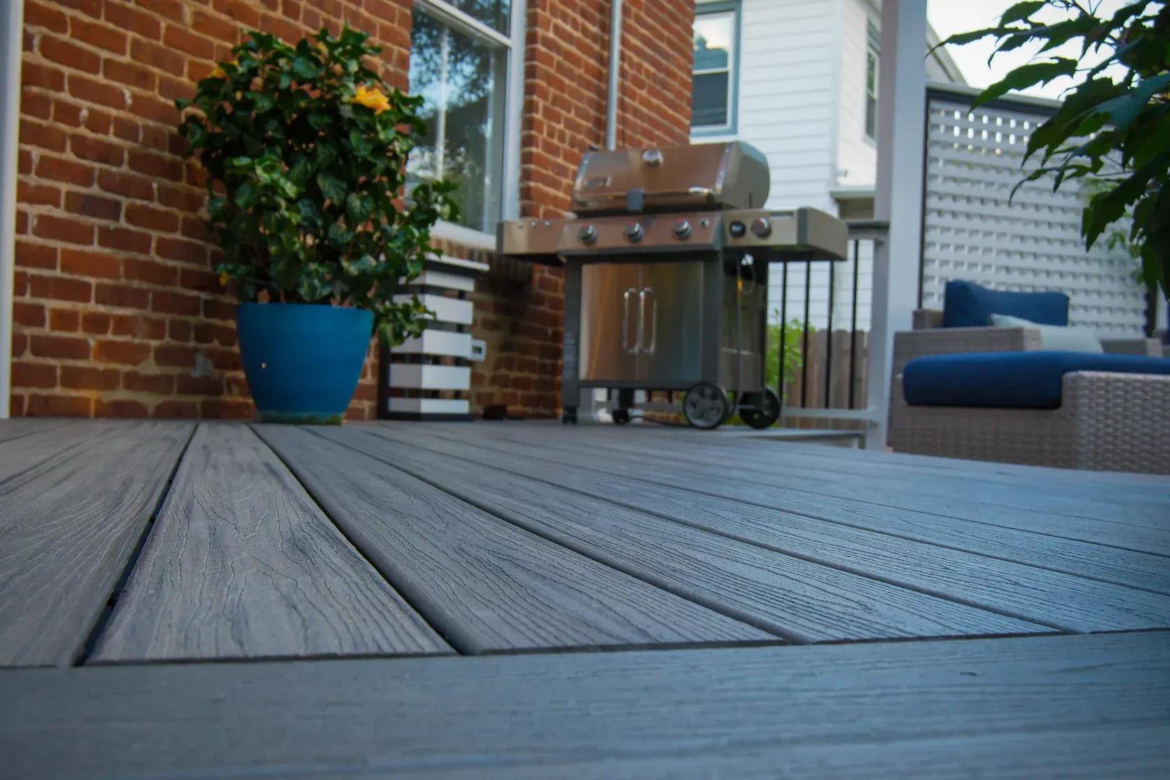 Composite deck with a grill and outdoor furniture. Brick house, blue plant pot.