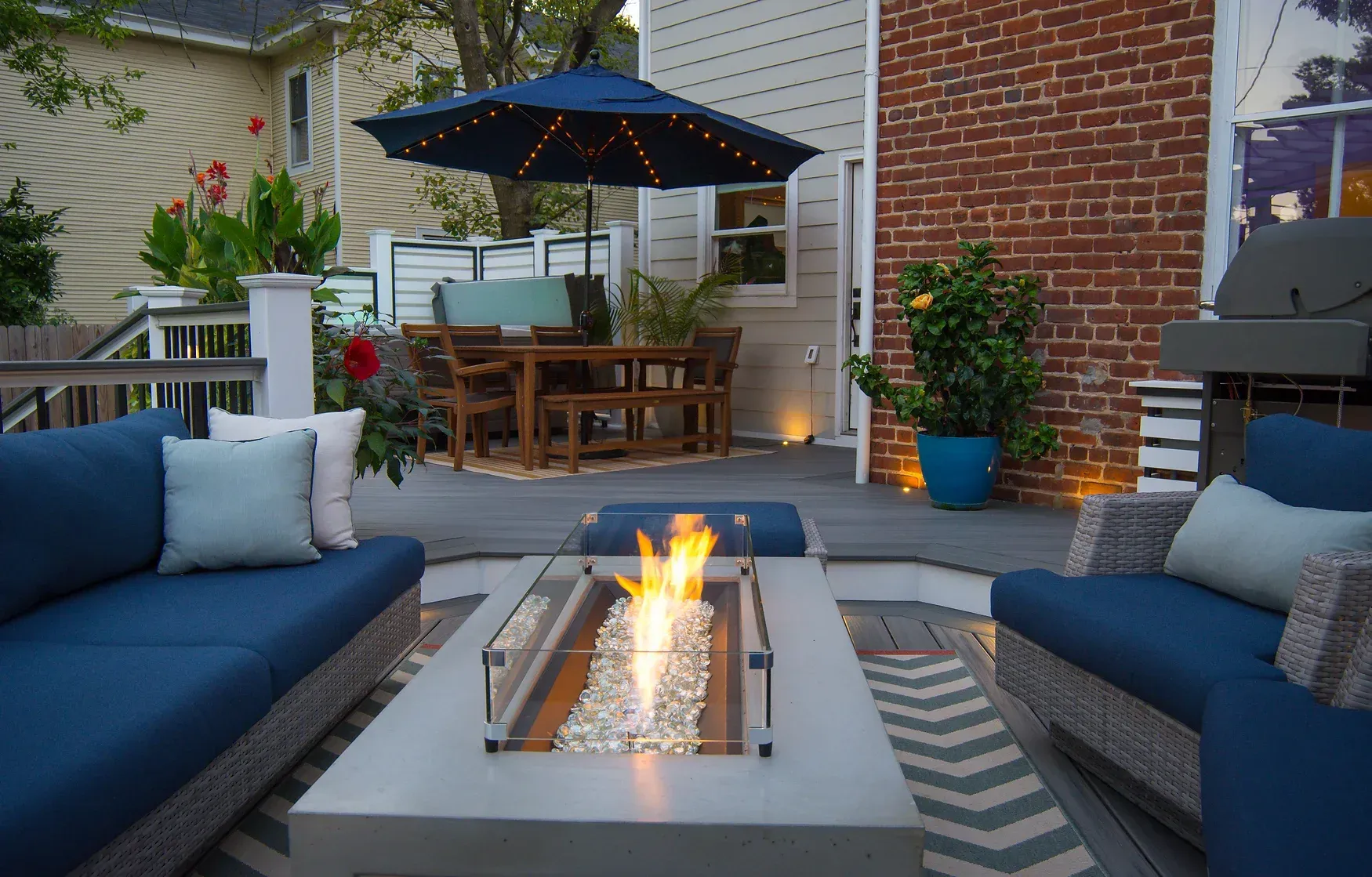 Outdoor living space with blue couches, fire pit, dining table, and umbrella.