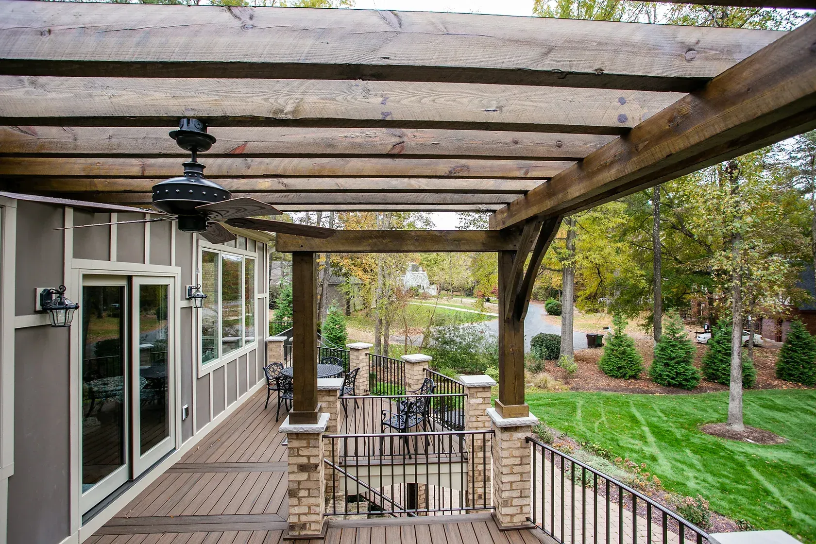 Wooden pergola over a deck with a fan, overlooking a lawn and trees.