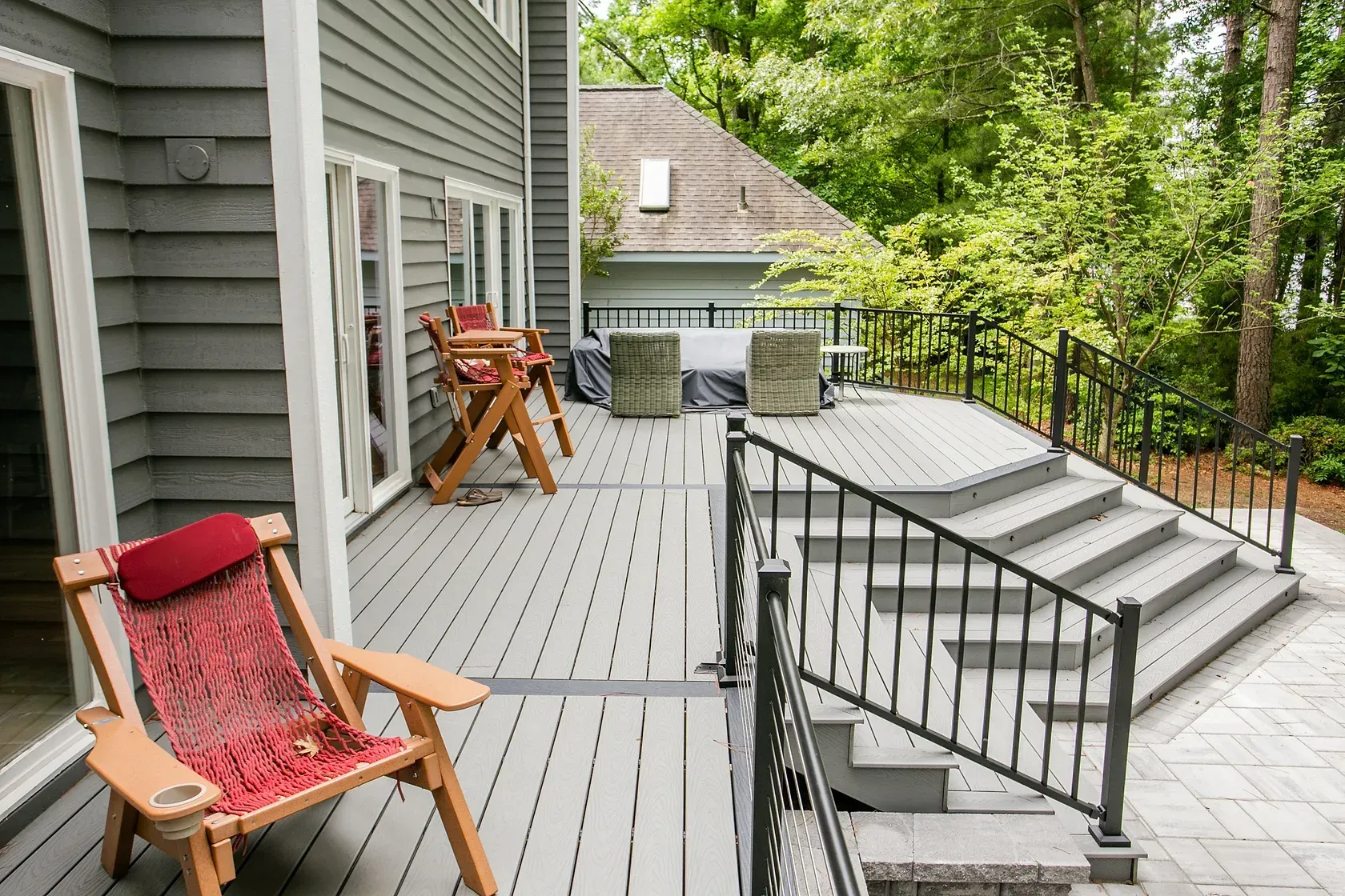 Wooden deck with outdoor seating and stairs leading to a stone patio, next to a gray house.