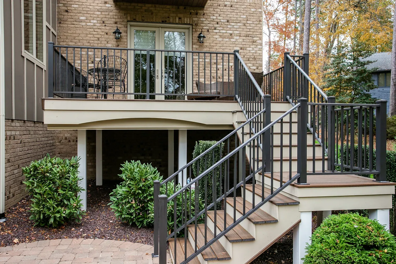 Exterior of a house with a deck and stairs. Tan and brown hues, metal railings, and landscaping.