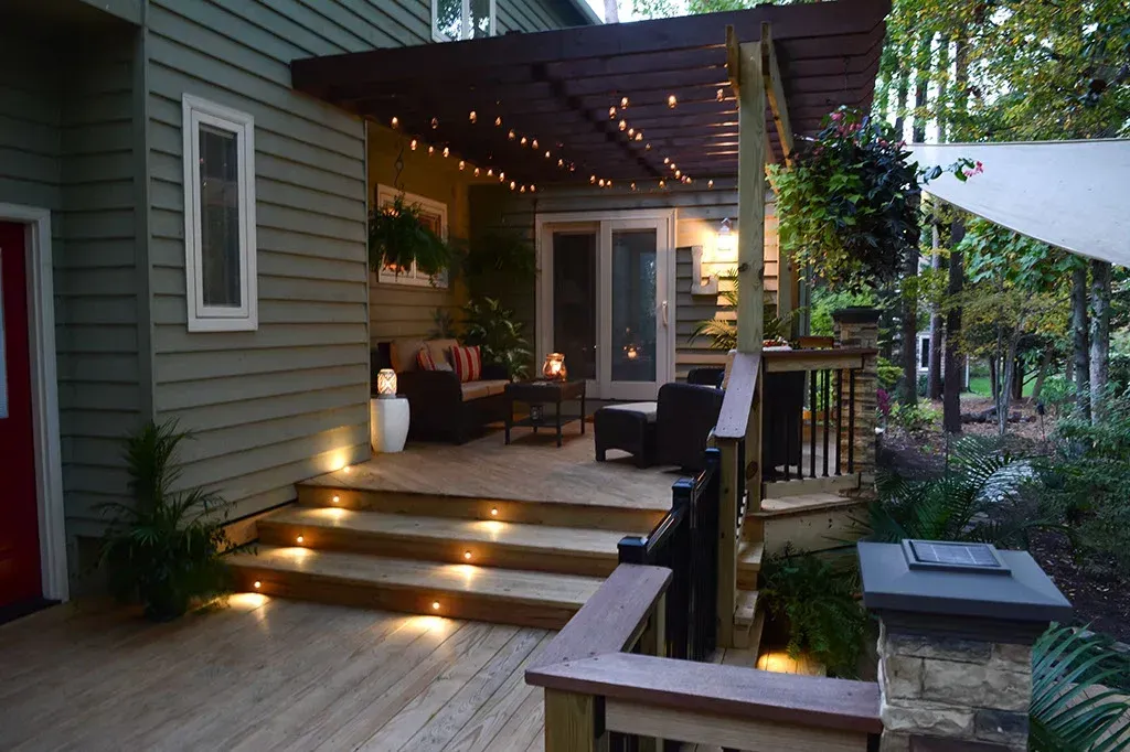 Wooden deck with string lights, steps, and chairs beneath a pergola.