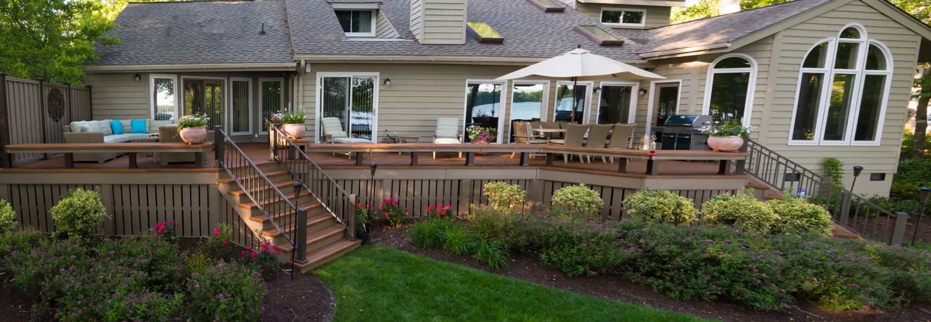 Backyard deck of a house with seating areas, landscaping, and a grill.