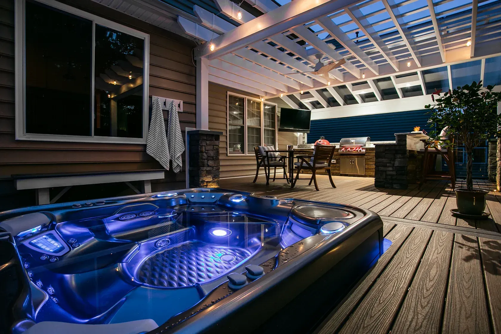 Outdoor deck with hot tub, string lights, pergola, and dining area at dusk.